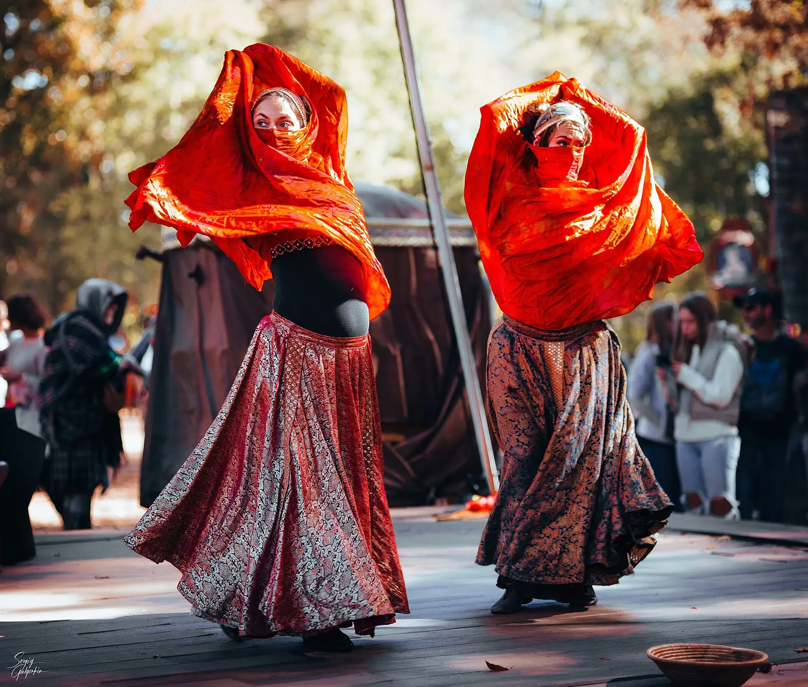 Two dancers in flowing orange veils and long skirts perform on a wooden stage at the Carolina Renaissance Festival in Huntersville