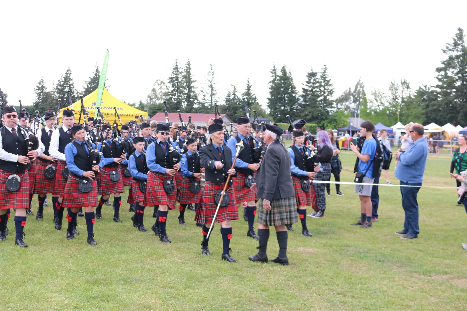 Pipers and drummers in kilts and glengarry caps line up on the field at the Hororata Highland Games in New Zealand
